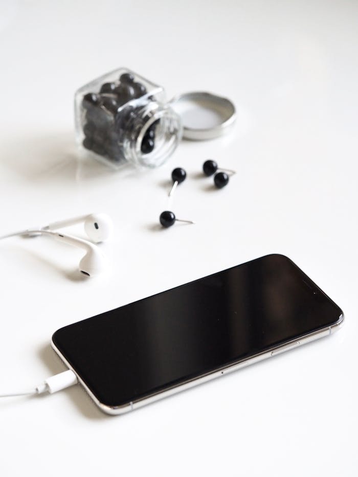Minimalist arrangement of smartphone, earbuds, jar, and pushpins on a white background.
